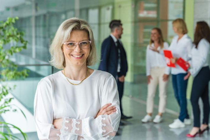 Smiling businesswoman with crossed arms in a bright, modern office environment.