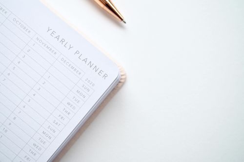A stylish yearly planner open to a 2020 calendar page, accompanied by a golden pen on a clean white surface.