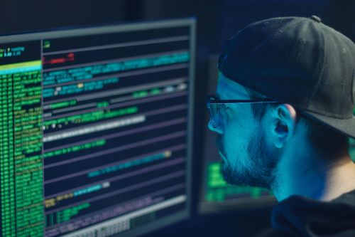 A cybersecurity expert inspecting lines of code on multiple monitors in a dimly lit office.