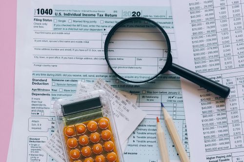 Magnifying glass, calculator, pencils on tax forms with pink background. Ideal for finance or education themes.