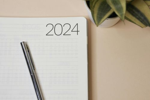 Minimalist 2024 planner with pen and indoor plant on a peach-colored background for productivity inspiration.