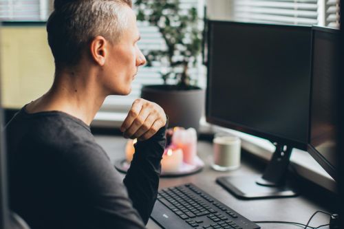 Person working remotely at a desk with a computer and candles, creating a cozy home office atmosphere.
