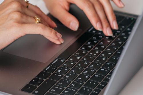 Hands of a woman typing on a laptop keyboard indoors, showcasing rings and fashion.
